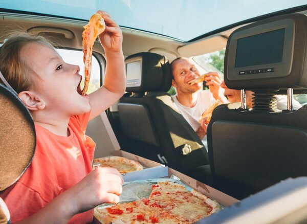 father and daughter eating pizza in the car