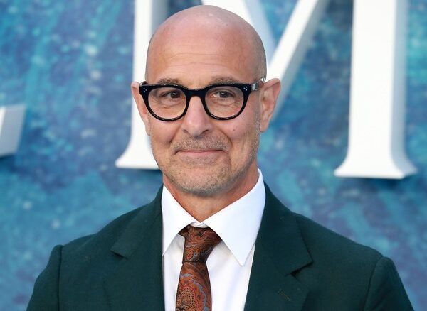 Stanley Tucci smiles in glasses and suit