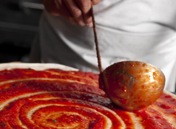 chef spreading sauce on pizza